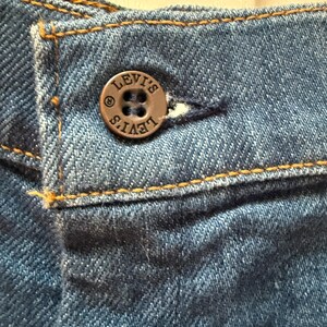 May include: Close-up of a blue denim jean with a brown button that says "LEVI'S" in a circular design.