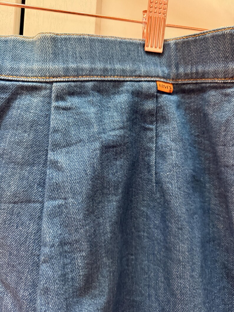 May include: A close-up of the back waistband of a pair of blue denim jeans with a brown Levi's label.
