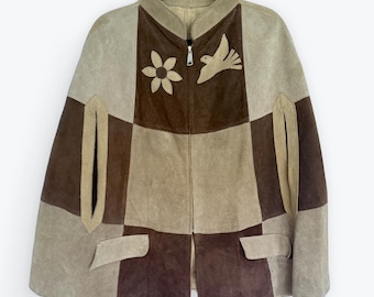 May include: A patchwork suede cape in shades of brown and tan, featuring a zip-up front and a high collar. The cape is adorned with a flower and bird applique. It has two front pockets and a unique design.