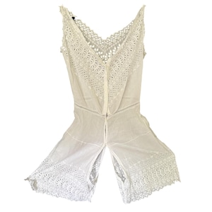 May include: White eyelet romper with a V-neckline and delicate floral cutouts. The sleeveless garment features a button-up front and open leg design. The fabric is lightweight and airy, perfect for warm weather.