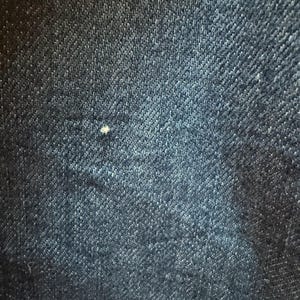 May include: Close-up of a dark blue denim fabric with a subtle diagonal weave pattern.