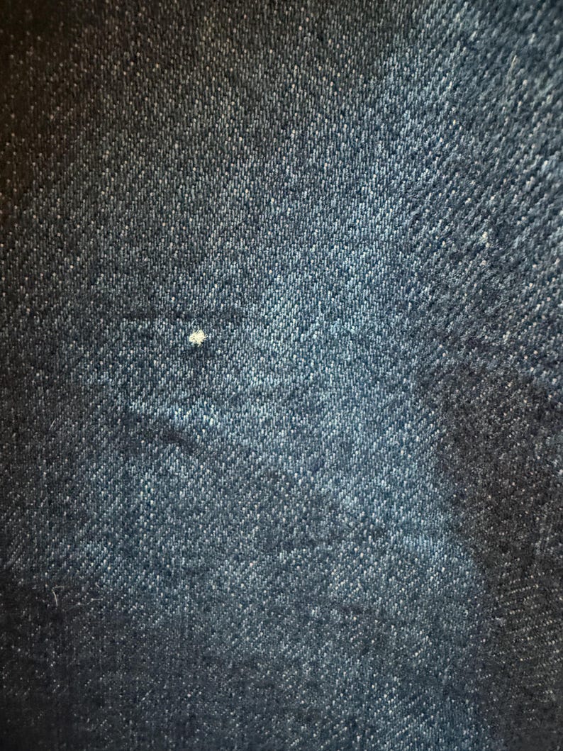 May include: Close-up of a dark blue denim fabric with a subtle diagonal weave pattern.