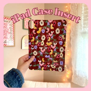 May include: An iPad case insert featuring a floral design. The case has a deep red base, adorned with a repeating pattern of colourful flowers in yellow, pink, purple, and white. The text "iPad Case Insert" is at the top.