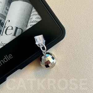 May include: A silver disco ball charm attached to a clear plastic clip. The charm is hanging from a black e-reader.