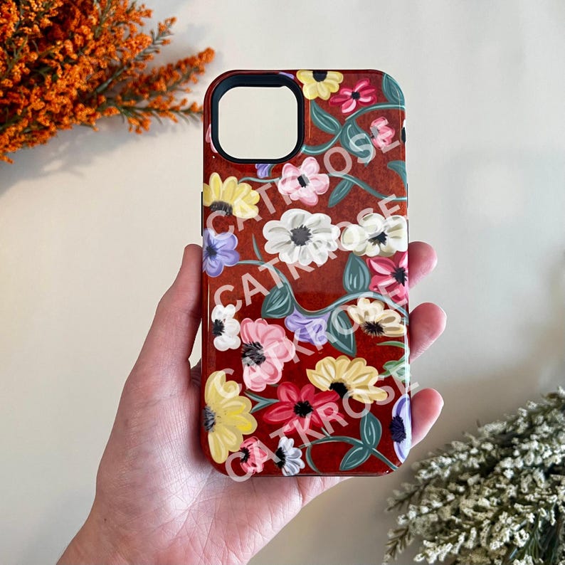 Op de afbeelding: Een rode telefoonhoes met een bloemenpatroon. De bloemen zijn geel, roze, wit en paars. De hoes heeft een zwarte camera-uitsparing.