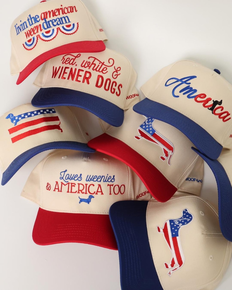 May include: A collection of cream-colored baseball caps with red and blue accents. Each cap features patriotic text and dachshund dog graphics. The phrases include "Livin' the American Ween Dream" and "Red, White & Wiener Dogs."