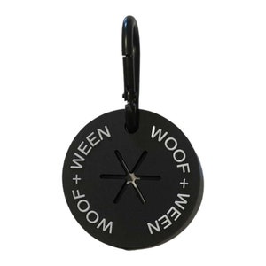 May include: Black round dog poo bag dispenser with a silver carabiner clip. The dispenser has the text "Woof + Ween" printed around the edge in white.