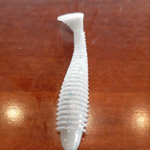 May include: White soft plastic fishing lure with a ribbed body and blue glitter accents.
