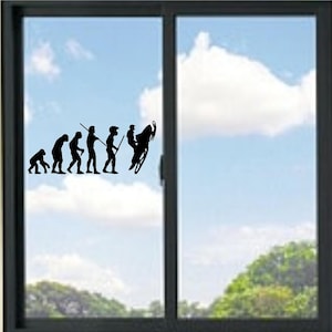May include: A black vinyl decal applied to a window, featuring the evolution of humanity sequence. The design progresses from a primate to a human, ending with a figure riding a snowmobile in a wheelie position, all in a solid black silhouette.