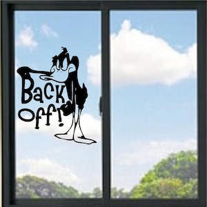 Può includere: Un adesivo in vinile nero applicato su una lastra di vetro. Il design raffigura un personaggio di un'anatra dei cartoni animati con un'espressione severa, appoggiato al testo "Back Off!" scritto in un carattere nero, audace e stilizzato.
