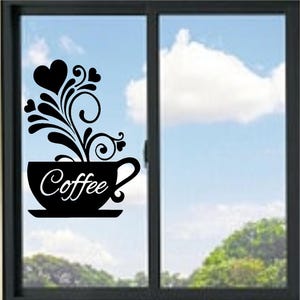 May include: A black vinyl window decal featuring a coffee cup silhouette with the word Coffee written in white script. Above the cup, black swirling lines and heart shapes rise like steam, creating a decorative graphic design on the glass.