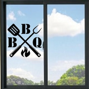 May include: A black vinyl decal applied to a glass window, featuring a crossed spatula and barbecue fork graphic. The letters B, B, and Q are positioned around the utensils, accompanied by a small flame icon at the bottom center of the design.