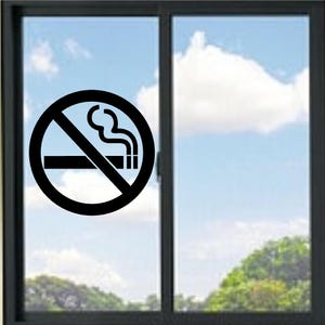 Puede incluir: Un adhesivo circular negro de prohibido fumar aplicado sobre un cristal de ventana. El gráfico muestra un cigarrillo estilizado con una columna de humo que sale del extremo, tachado por una línea diagonal dentro de un borde circular grueso.