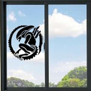 Puede incluir: Un adhesivo de vinilo negro que presenta la silueta estilizada de una criatura xenomorfa en posición agachada, encerrada dentro de un borde circular en forma de engranaje, aplicado sobre la superficie de un cristal con vista al cielo y árboles.