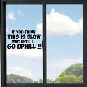 May include: A black vinyl decal applied to a window pane featuring the text IF YOU THINK THIS IS SLOW WAIT UNTIL I GO UPHILL !! in a bold, sans-serif font. The sticker is positioned on the left side of a dark-framed sliding glass window.