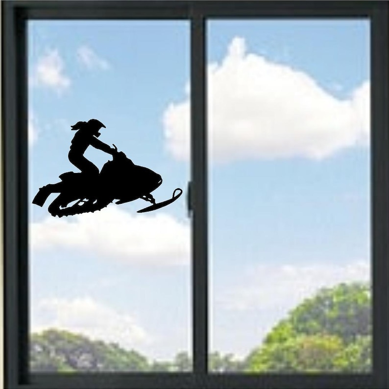 May include: A black silhouette of a person riding a snowmobile, set against a backdrop of a blue sky with clouds and a green landscape. The snowmobile is in mid-air, suggesting movement and speed. The image is framed by a window.