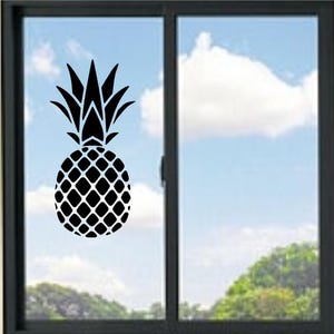 Op de afbeelding: Een zwarte vinylsticker van een ananassilhouet aangebracht op een glazen raam. Het ontwerp toont een gedetailleerd vruchtlichaam met een ruitpatroon en scherpe, puntige bladeren, wat zorgt voor een hoog contrast op het heldere glas.