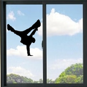 May include: A black silhouette of a breakdancer performing a handstand on a window. The dancer's legs are extended, and the body is in a dynamic pose. The background shows a blue sky with clouds and a green landscape.
