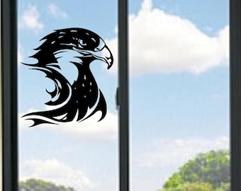 May include: A black eagle head decal is affixed to a window. The eagle's head is in profile, with sharp details and a stylized design. The background shows a blue sky with clouds and green trees.