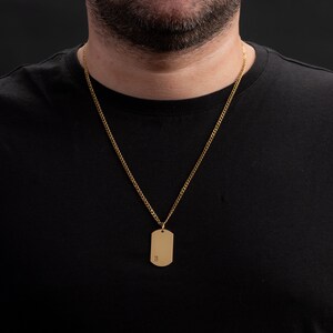 May include: A gold chain necklace with a gold dog tag pendant. The dog tag has the letter "H" engraved on it.