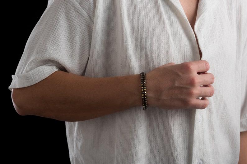 Men's bracelet with black hematite beads and gold-tone highlights, secured by an oxidized 925 sterling silver clasp and chain, offering adjustable sizing and a sleek design.