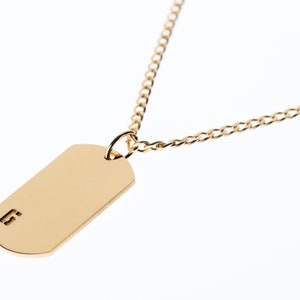 May include: A gold chain necklace with a gold dog tag pendant. The dog tag has the number "6" engraved on it.