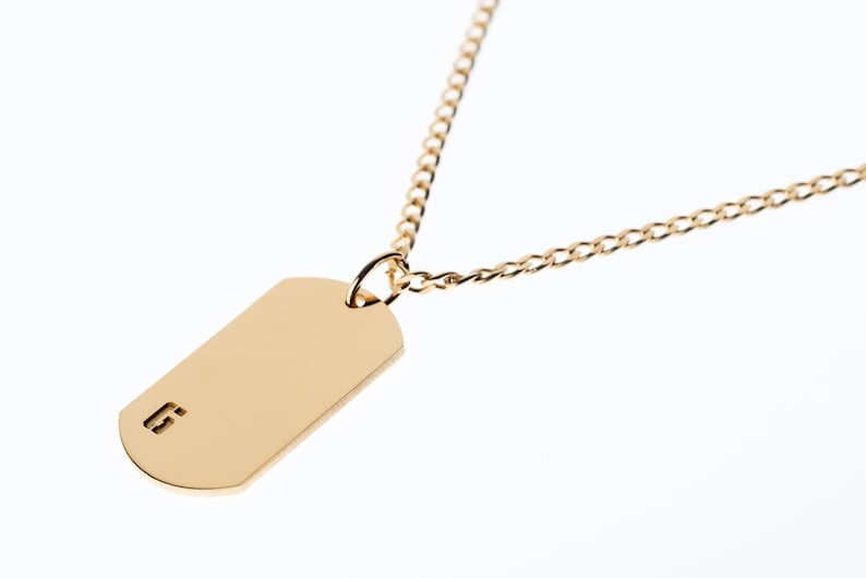May include: A gold chain necklace with a gold dog tag pendant. The dog tag has the number "6" engraved on it.