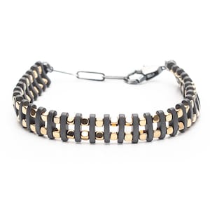 Mens bracelet with black hematite beads and gold-tone highlights, secured by an oxidized 925 sterling silver clasp and chain, offering adjustable sizing and a sleek design.