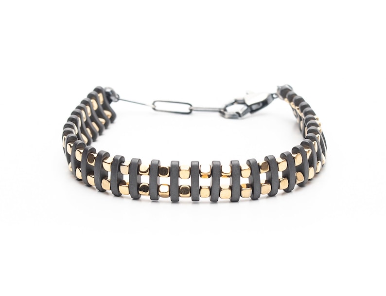 Mens bracelet with black hematite beads and gold-tone highlights, secured by an oxidized 925 sterling silver clasp and chain, offering adjustable sizing and a sleek design.