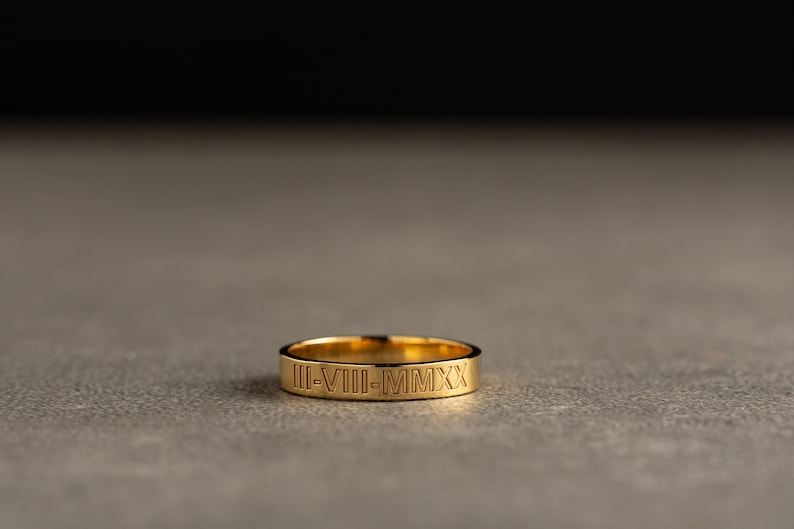 May include: A gold band ring with the inscription "II-VIII-MMXX" engraved on the outside.