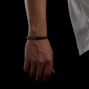 Men's bracelet with black hematite beads and gold-tone highlights, secured by an oxidized 925 sterling silver clasp and chain, offering adjustable sizing and a sleek design.
