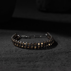 Men's bracelet with black hematite beads and gold-tone highlights, secured by an oxidized 925 sterling silver clasp and chain, offering adjustable sizing and a sleek design.