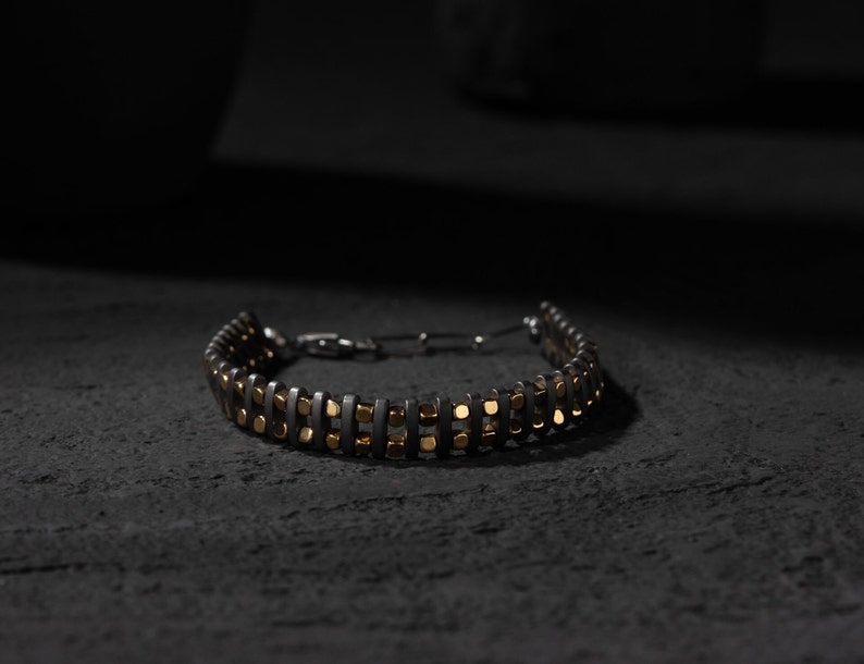 Men's bracelet with black hematite beads and gold-tone highlights, secured by an oxidized 925 sterling silver clasp and chain, offering adjustable sizing and a sleek design.