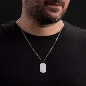 May include: A silver chain necklace with a silver dog tag pendant. The dog tag has the letter "B" engraved on it.