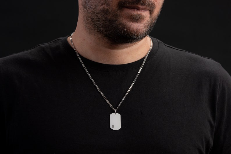 May include: A silver chain necklace with a silver dog tag pendant. The dog tag has the letter "B" engraved on it.