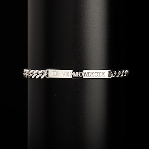 K&ouml;nnte beinhalten: Silberarmband mit einer rechteckigen Plakette, die mit den r&ouml;mischen Ziffern "IX-VII-MCMXCIX" graviert ist.