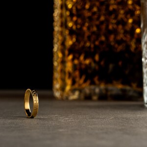 May include: A gold ring with a textured surface and engraved lettering. The ring is lying on a gray surface.