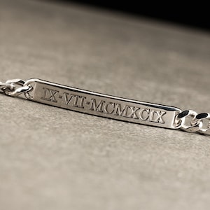 K&ouml;nnte beinhalten: Silberarmband mit einer rechteckigen Plakette, die mit dem r&ouml;mischen Datumszeichen "IX-VII-MCMXCIX" graviert ist.
