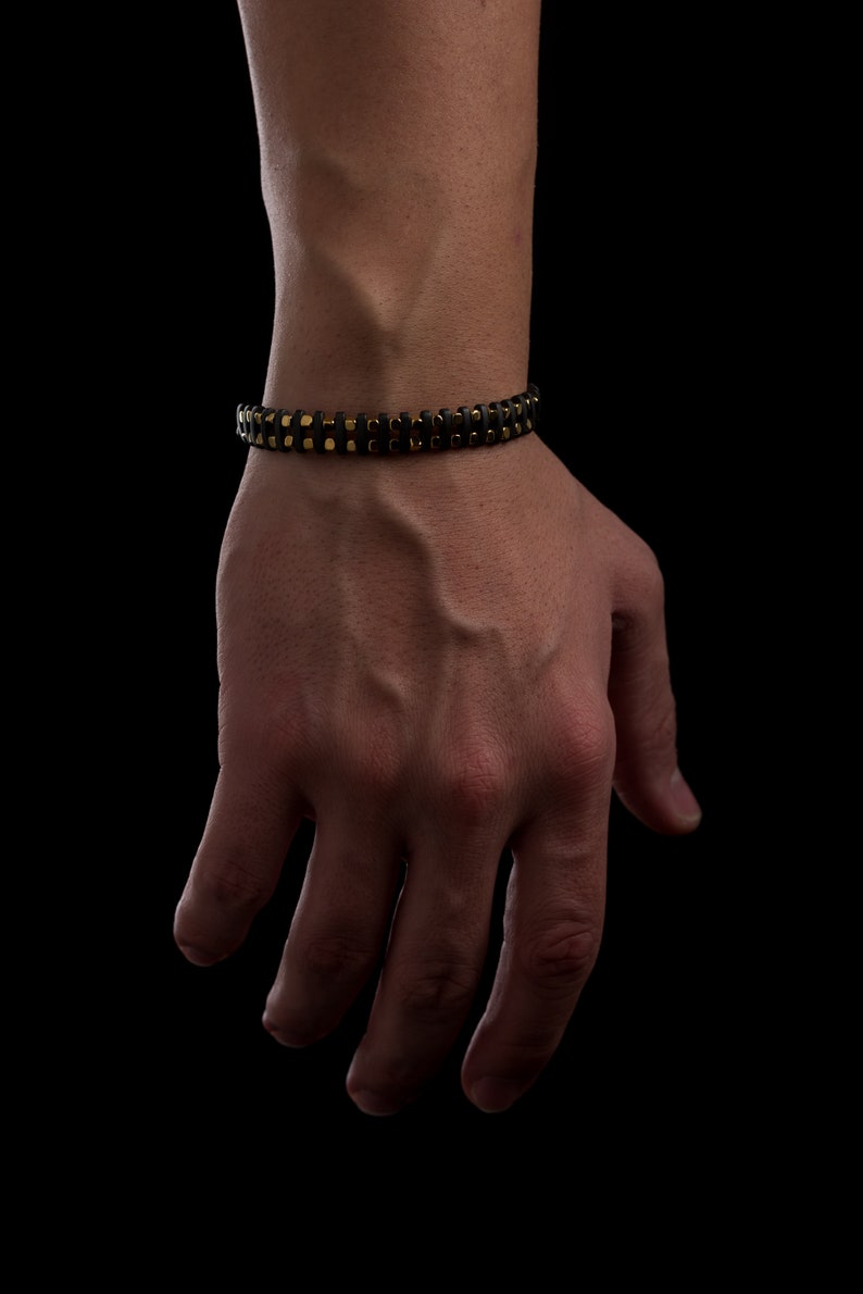 Men's bracelet with black hematite beads and gold-tone highlights, secured by an oxidized 925 sterling silver clasp and chain, offering adjustable sizing and a sleek design.