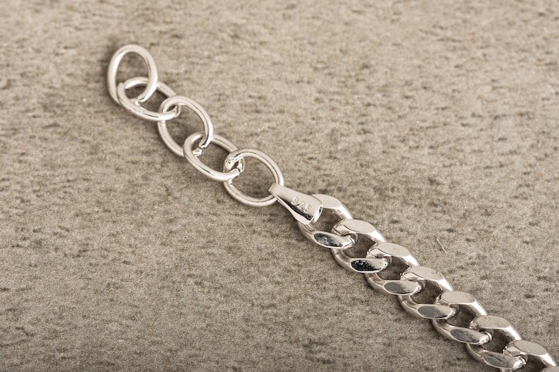 K&ouml;nnte beinhalten: Nahaufnahme einer silbernen Kettenkette mit einem Karabinerverschluss. Die Kette besteht aus dicken, ineinandergreifenden Gliedern.