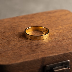 May include: A gold ring with Roman numerals engraved around the band. The ring is sitting in a wooden box.