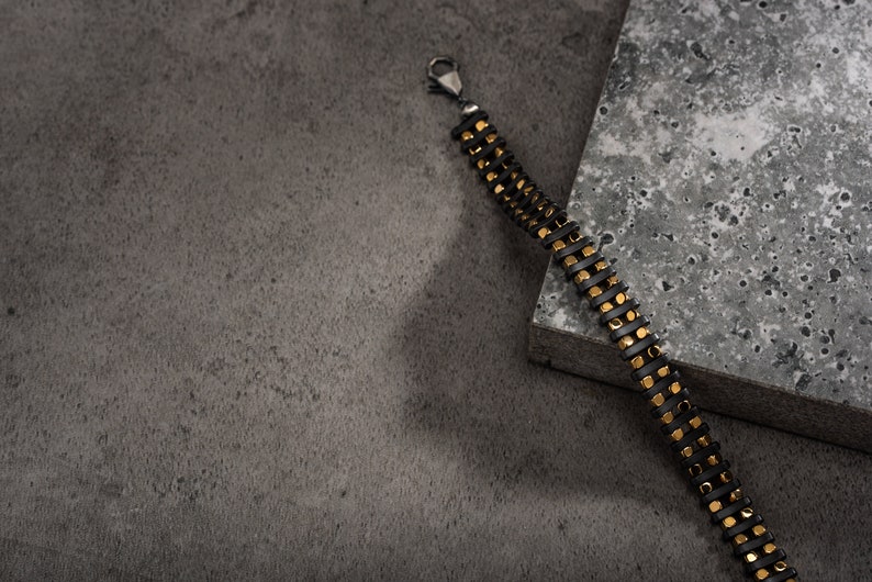 Men's bracelet with black hematite beads and gold-tone highlights, secured by an oxidized 925 sterling silver clasp and chain, offering adjustable sizing and a sleek design.