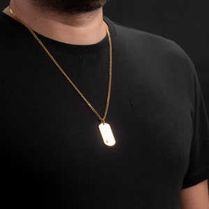 May include: A gold chain necklace with a gold dog tag pendant.