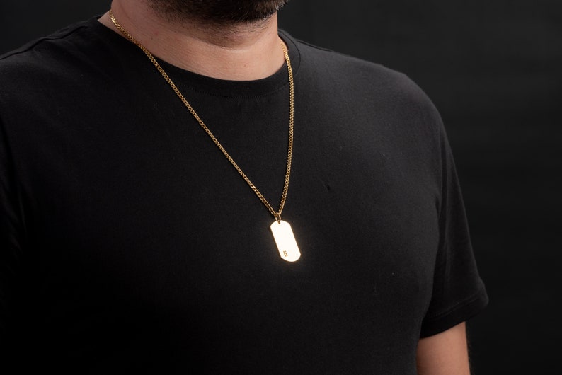 May include: A gold chain necklace with a gold dog tag pendant.