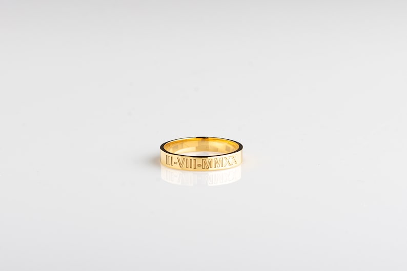 May include: A gold band ring with the inscription "III-VIII-MMXX" engraved on the outside.