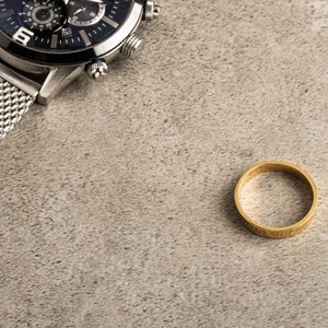 May include: A silver watch with a black face and a mesh band, and a gold ring on a gray background.