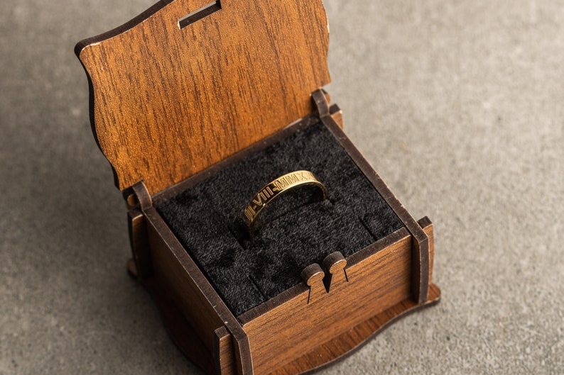 May include: A gold ring with Roman numerals engraved on it, inside a wooden box with a black velvet lining.