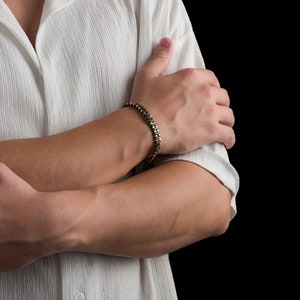 Men's bracelet with black hematite beads and gold-tone highlights, secured by an oxidized 925 sterling silver clasp and chain, offering adjustable sizing and a sleek design.