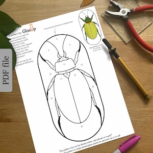 Op de afbeelding: Een zwart-wit lijntekeningpatroon van een kever met genummerde secties. Het patroon is gelabeld "A pattern by GlasUp" en bevat instructies voor het maken van glas-in-loodstukken. De geschatte grootte van het patroon is 10 x 23 cm of 4 x 8,7 inch.