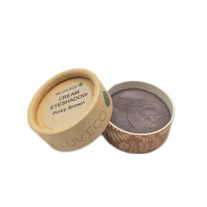 May include: A small, round container of pinky brown cream eyeshadow. The container is made of cardboard and has a label that reads "WE LUV ECO CREAM EYESHADOW Pinky Brown".